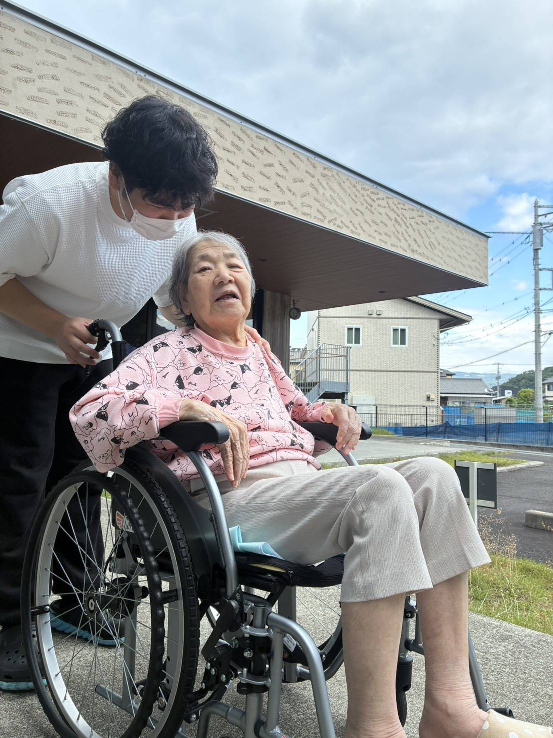 Comrade清水町のデイサービスで、職員が車椅子のご利用者様に寄り添いながら外の空気を楽しむ様子